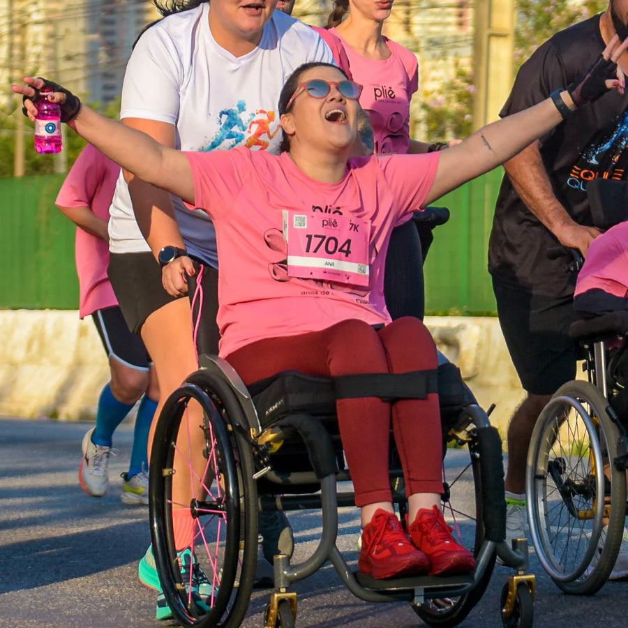 Mulher cadeirante comemorando a conclusão do percurso da Corrida Plié, um evento para todos os ritmos. 
